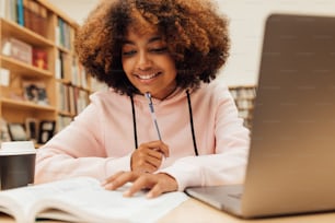 Young female in a school library working on laptop. Woman studying on school assignment.