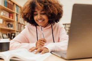 Jovem do sexo feminino em uma biblioteca da escola trabalhando em laptop. Mulher que estuda na tarefa escolar.