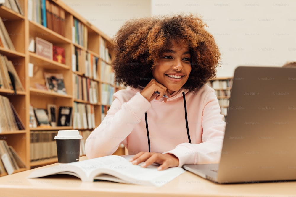 Chica sonriente con cabello rizado mirando la computadora portátil y preparando exámenes