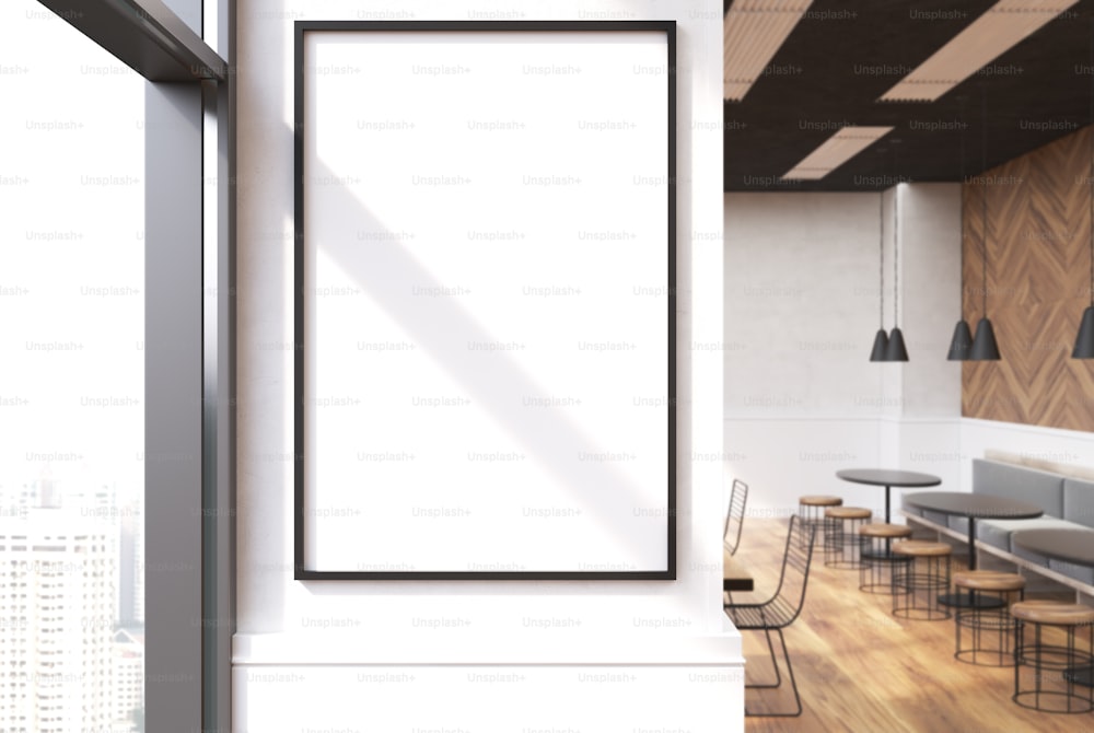 Close up of a vertical framed poster on a cafe wall. Large windows, white and wooden walls and round tables with sofas and stools. 3d rendering mock up