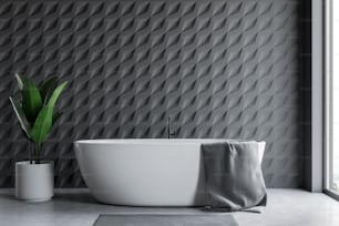 Intérieur de la salle de bain loft avec murs en carreaux gris, sol en béton, baignoire blanche avec serviette grise accrochée dessus et grande plante en pot. Rendu 3D