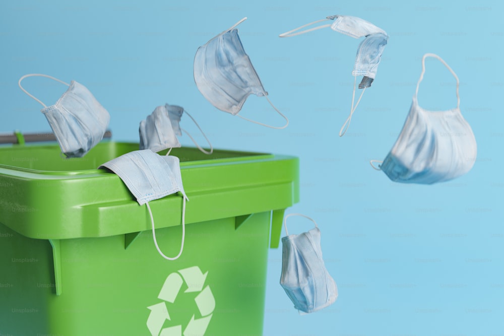 3D illustration of bunch of used face masks falling into recycling bin against blue background during pandemic