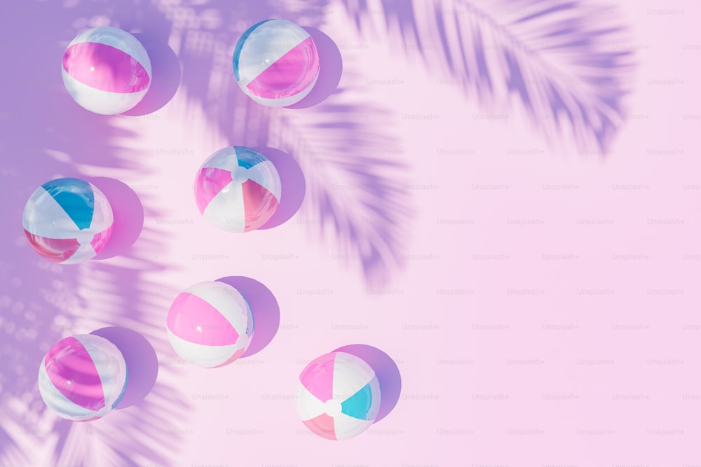 Top view 3D rendering of striped inflatable balls scattered on pink surface with shadow of palm tree branches on sunny day