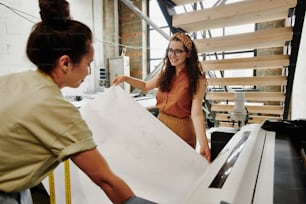 Two young contemporary fashion designers printing large sketch of new items of their seasonal collection before cutting them out