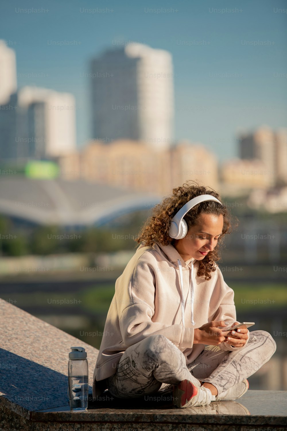 Joven mujer morena con auriculares y ropa deportiva que se desplaza por la música en línea mientras elige algo para escuchar durante el entrenamiento
