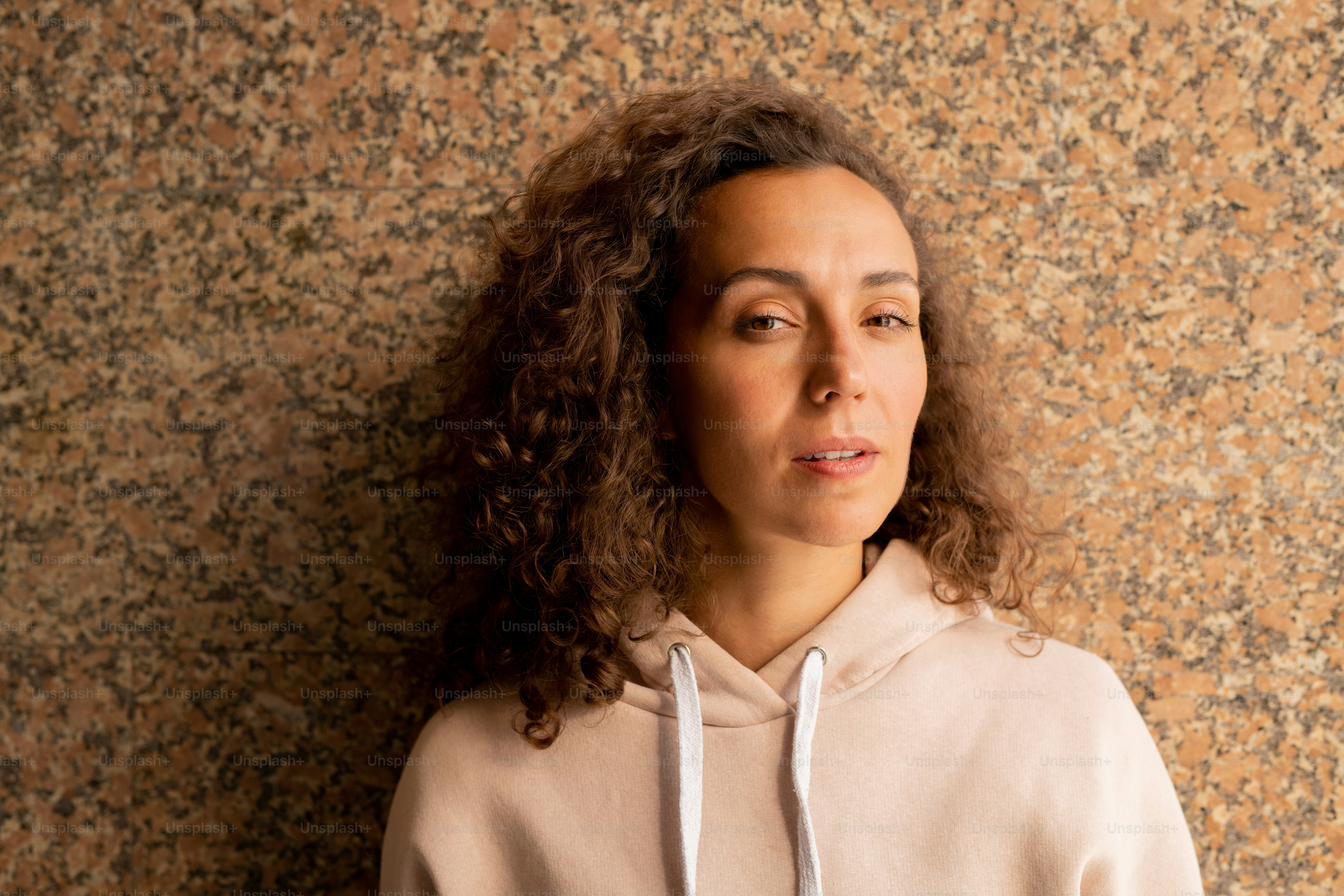 Young serious sportswoman with dark wavy hair standing against marble tiled structure or wall of building and looking at you