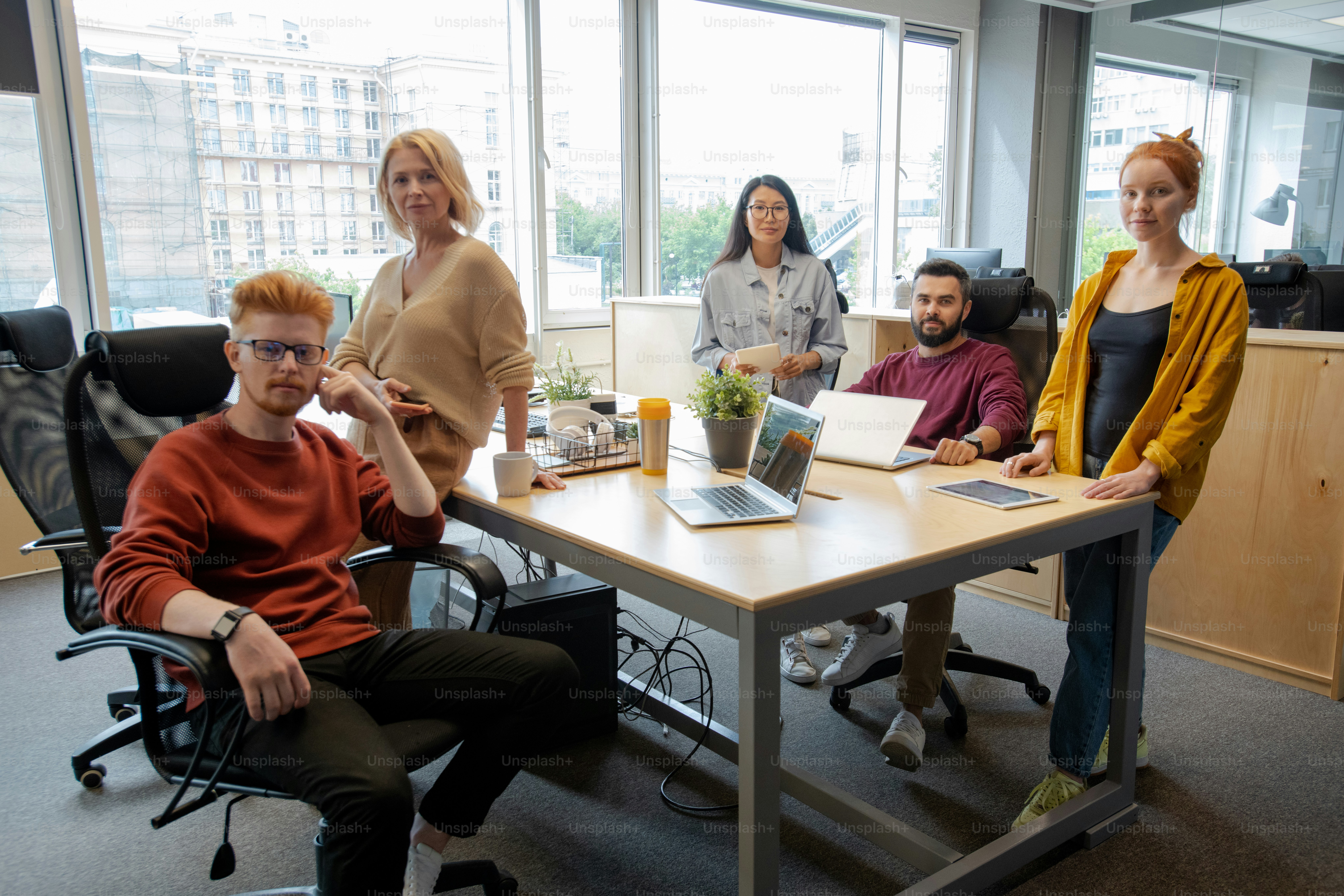 Group of intercultural business people gathered by table in office against window for brainstorming and discussion of ideas and strategies