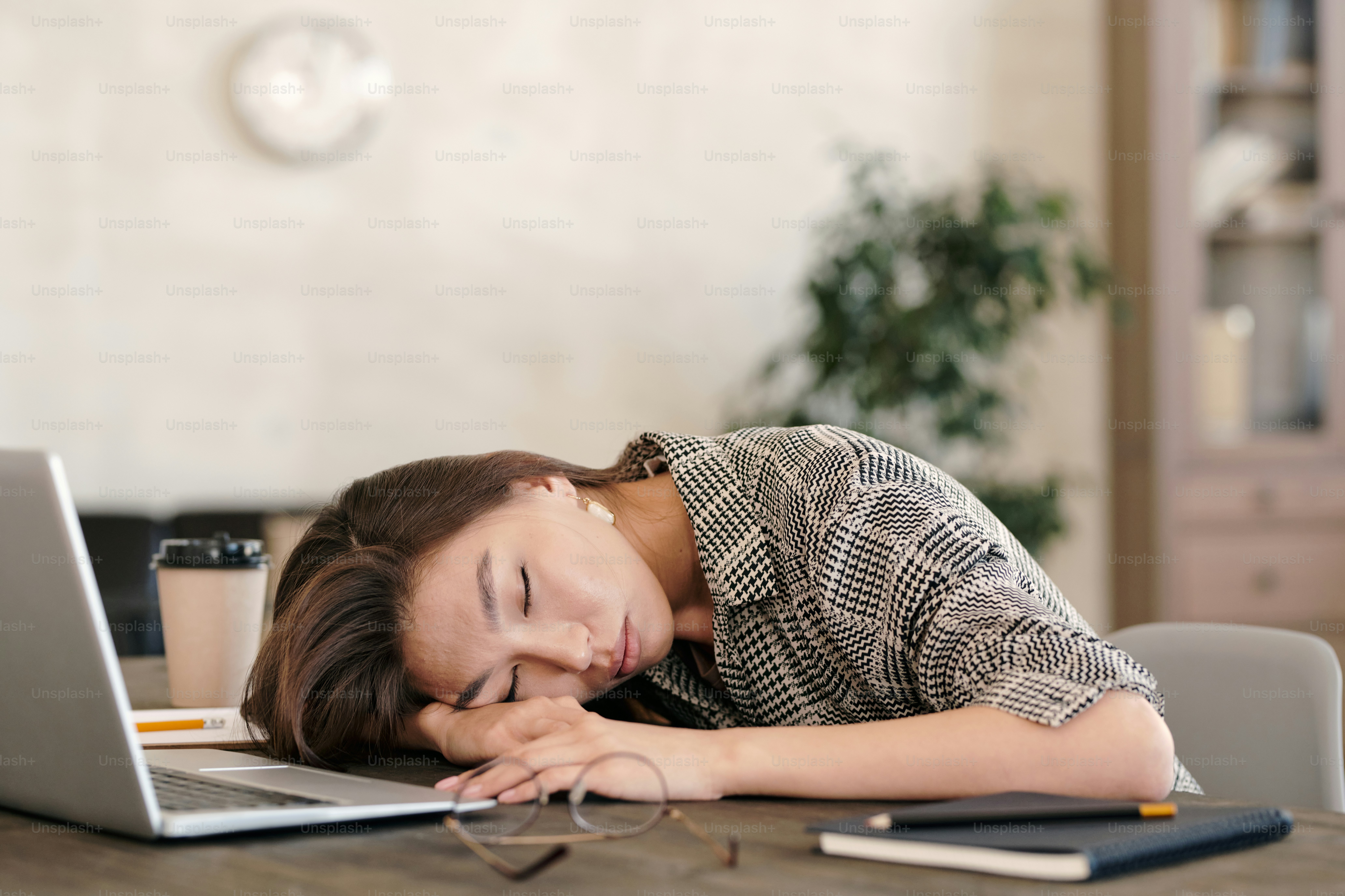 Young exhausted businesswoman in formalwear keeping her head on hand while napping in front of laptop after work in office environment