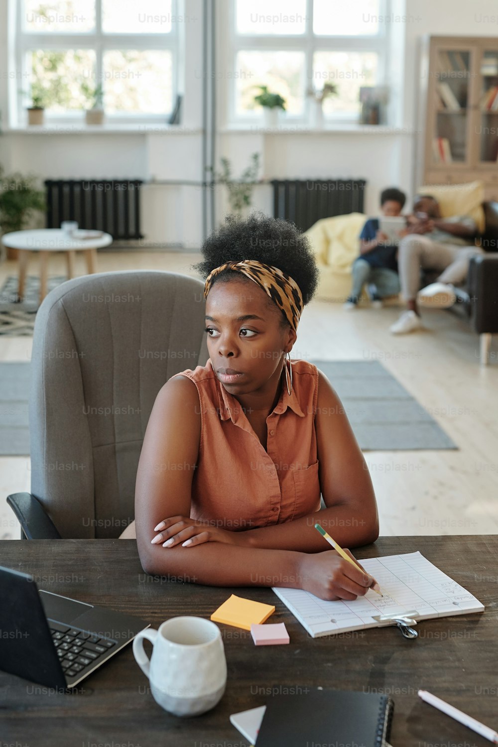 Pensive young businesswoman of African ethnicity in brown casual blouse and leopard print headband making notes in document by table