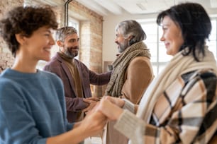 Young and senior men and women in casualwear greeting one another by handshake and looking at each other against home environment