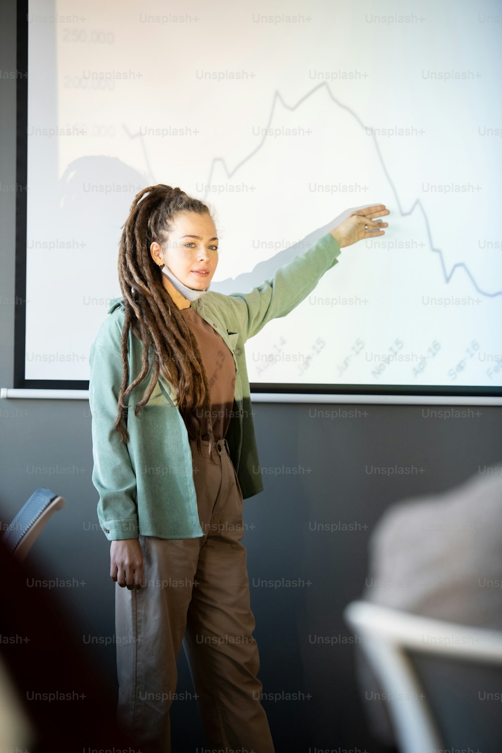 Une jeune coach d’affaires confiante en tenue décontractée explique le graphique sur tableau blanc lors d’une présentation à une conférence pour les économistes