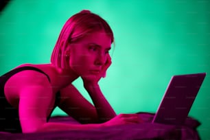 黒い下着を着た金髪の真面目な女の子が、朝や夕方にベッドでネットワークを見たり、オンラインビデオを見たりしながらノートパソコンのディスプレイを見ている