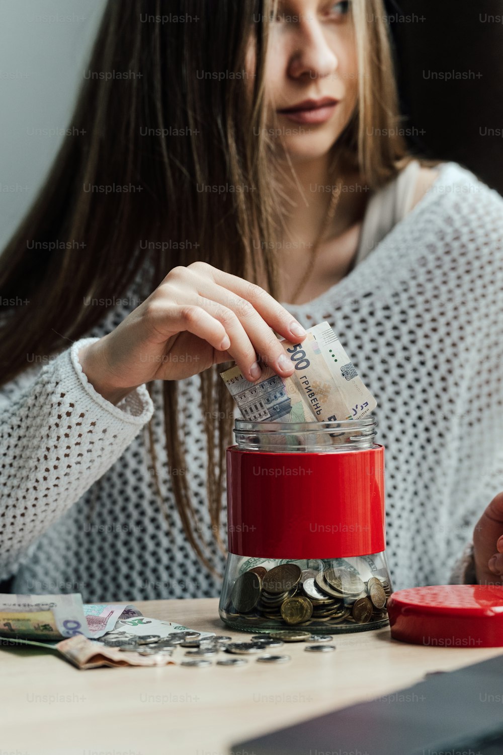 a woman putting money in a jar on top of a table