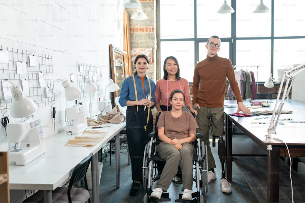 성공적인 현대 패션 디자이너와 캐주얼웨어를 입은 재단사 팀이 작업 장비를 갖춘 테이블 사이에 서 있습니다