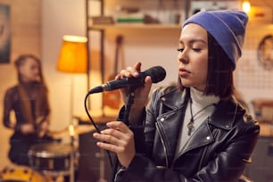 Young pretty woman in hat singing in microphone during the rehearsal with her group in studio