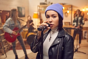 Giovane femmina con il microfono che canta davanti alla telecamera con la sua band sullo sfondo