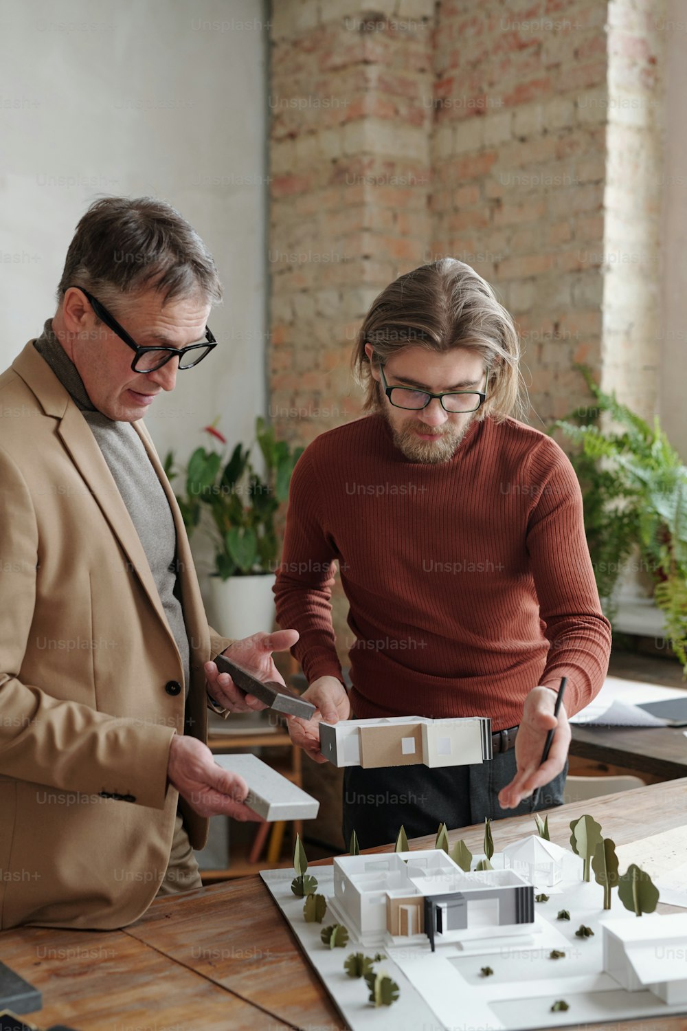 안경을 쓴 젊은 백인 건축가가 테이블에 서서 재료 샘플을 들고 상사에게 프로젝트를 발표하고 있다
