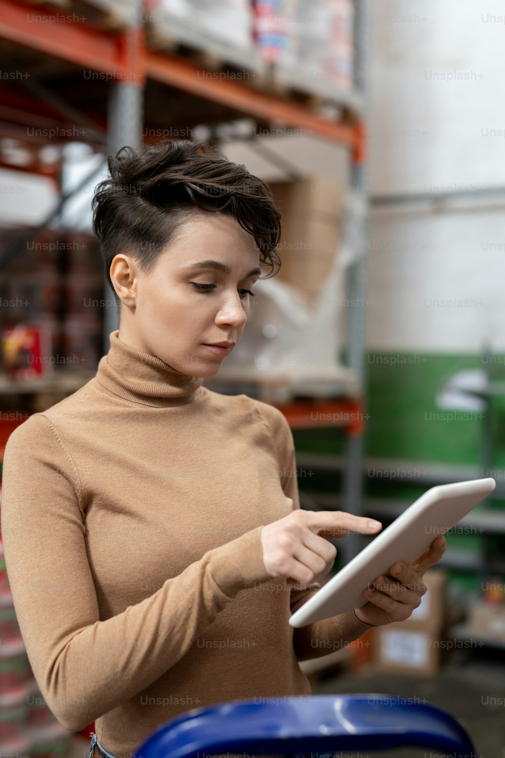 Serious attractive stock control manager with short hair standing at warehouse and using tablet while analyzing information about delivery