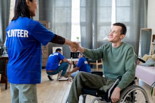 Young female volunteer shaking hand of man in a wheelchair