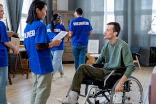 Une jeune bénévole en uniforme debout devant un homme en fauteuil roulant