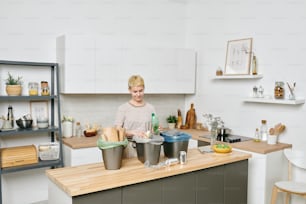 Mujer joven de pie junto a la mesa de la cocina mientras clasifica los desechos