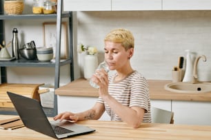 Young businesswoman sitting by table with laptop and drinking water