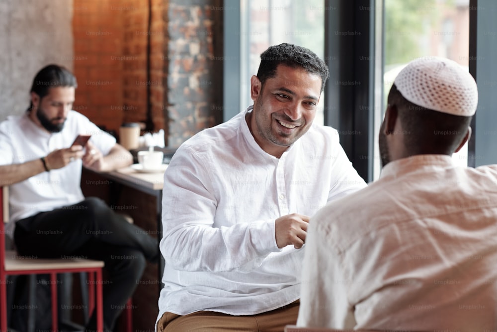 Homens muçulmanos positivos sentados no balcão do café e conversando juntos