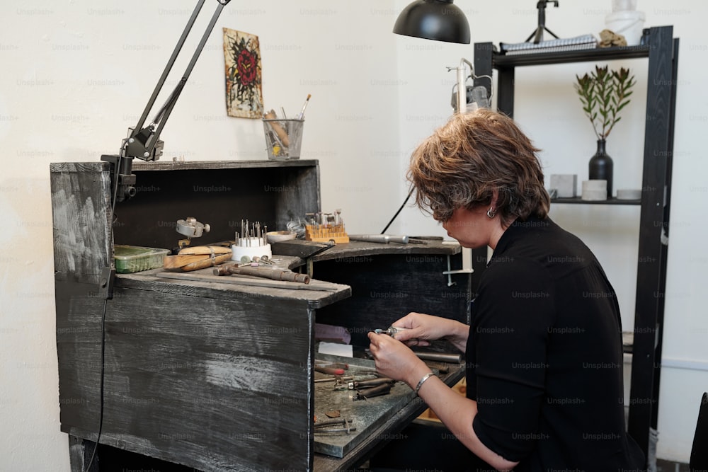Frau benutzt Schleifpolier, während sie in einer minimalistischen Werkstatt an einer neuen Schmuckkollektion arbeitet