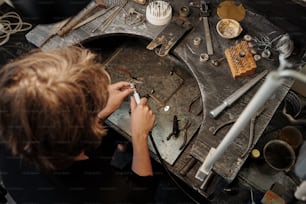 Visão de alto ângulo do joalheiro usando a ferramenta abrasiva durante o polimento do anel de prata na estação de trabalho