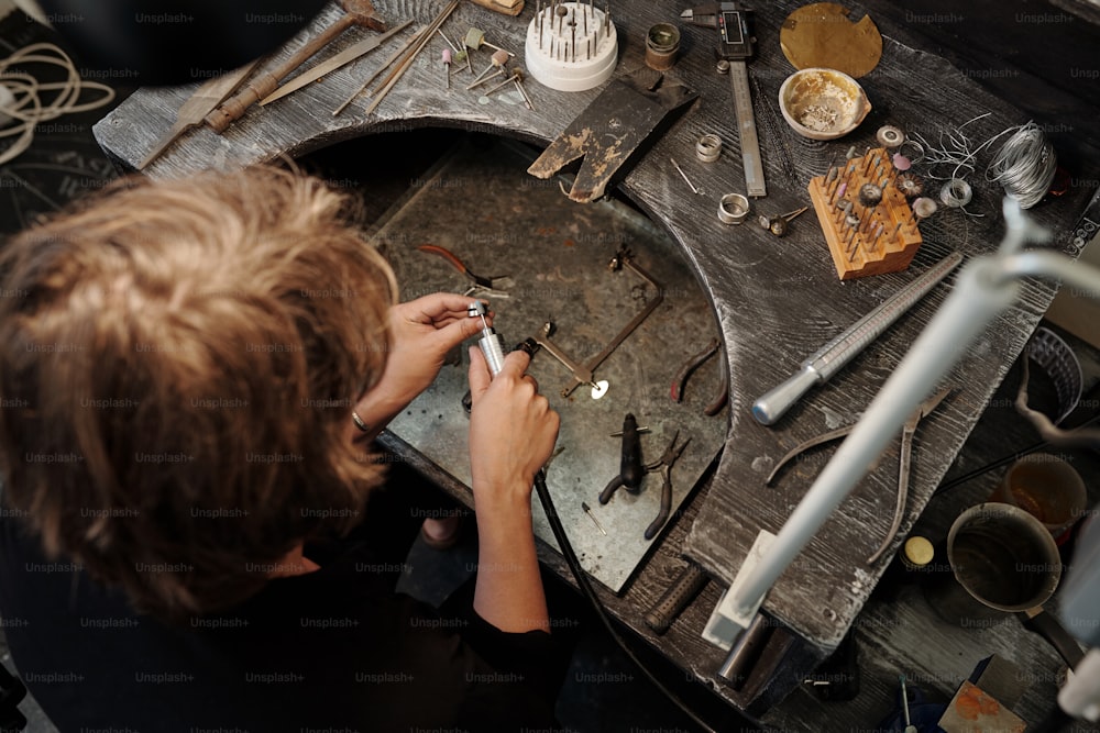 Hochwinkelansicht des Juweliers mit Schleifwerkzeug beim Polieren des Silberrings am Arbeitsplatz