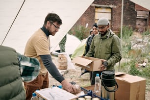 Bearded volunteer in yellow tshirt standing in food tent and giving food to refugees