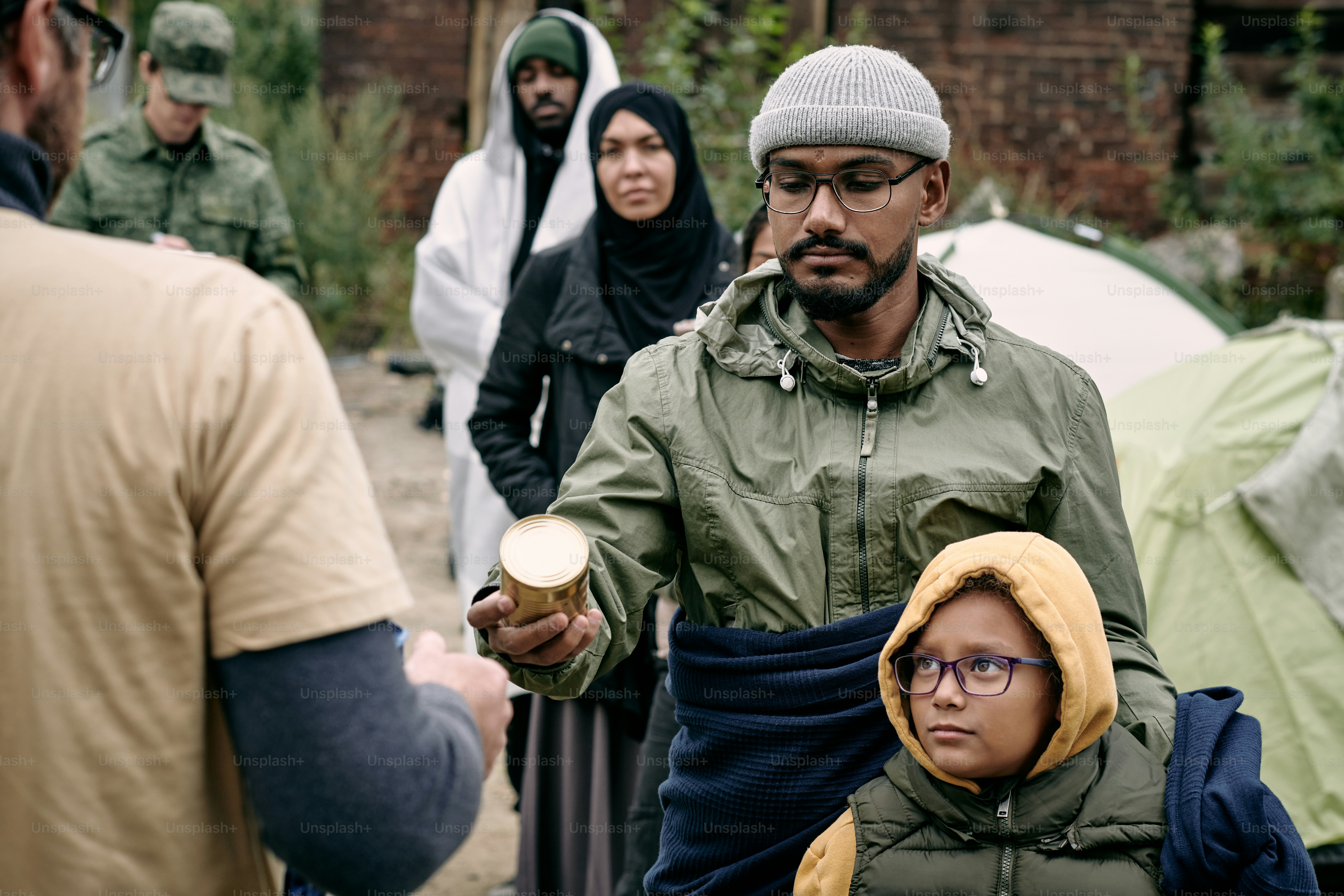 Arabian refugees standing in line while receiving food stocks from social worker, soldier controlling this process