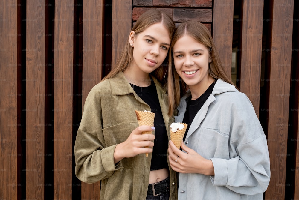 Two pretty teenage girls with icecream cones standing against building exterior