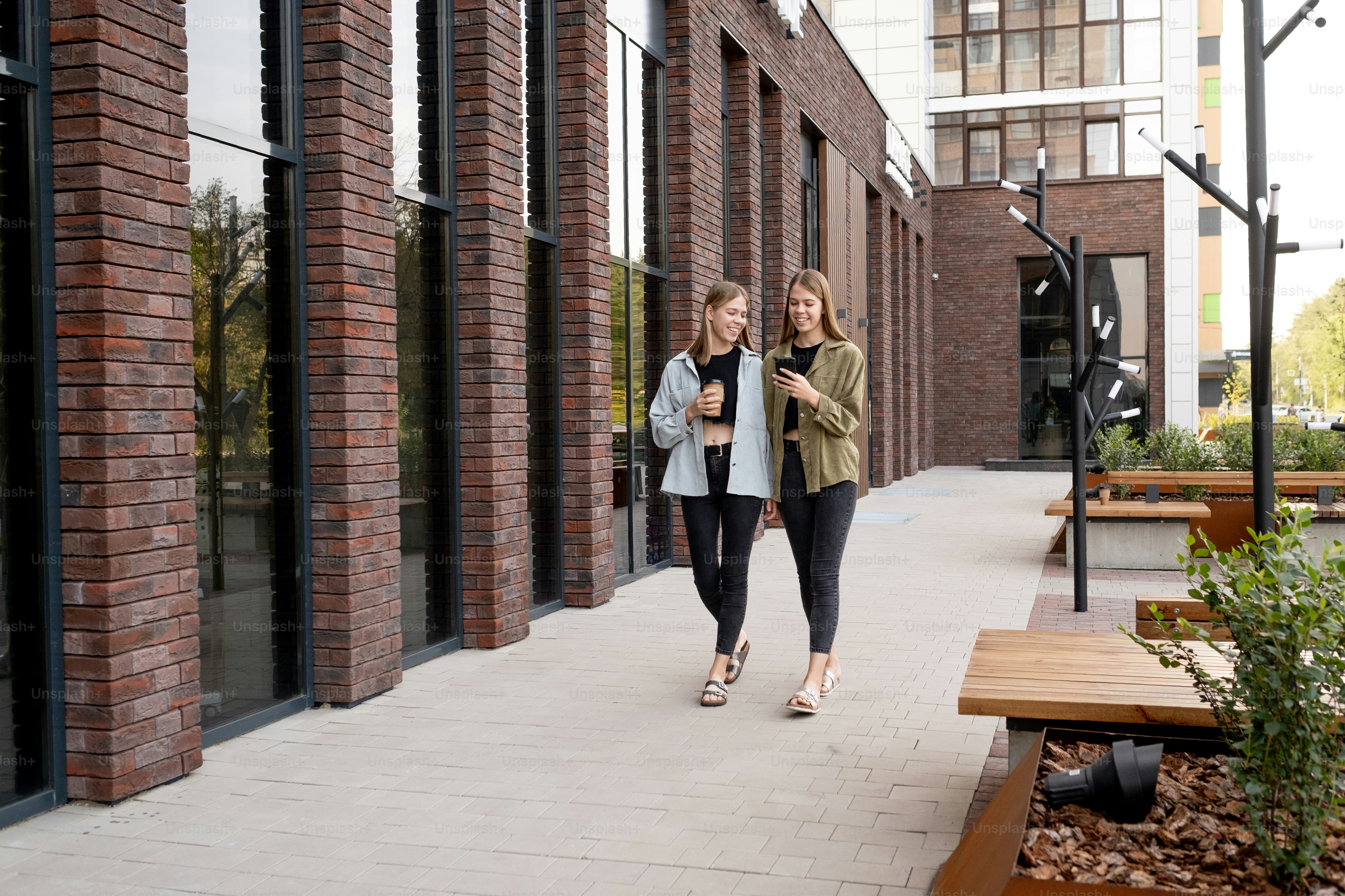 Teenage female twins watching video in smartphone while moving down road in urban environment