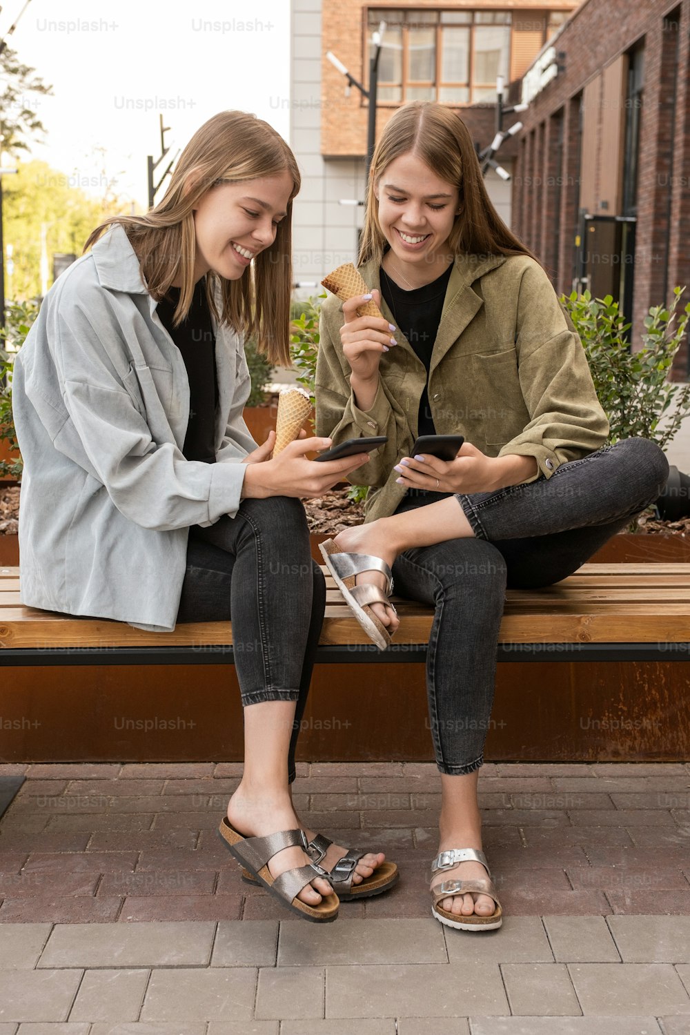 Zwei glückliche Mädchen mit Icecrean schauen sich ein neugieriges Video auf dem Smartphone in einer städtischen Umgebung an