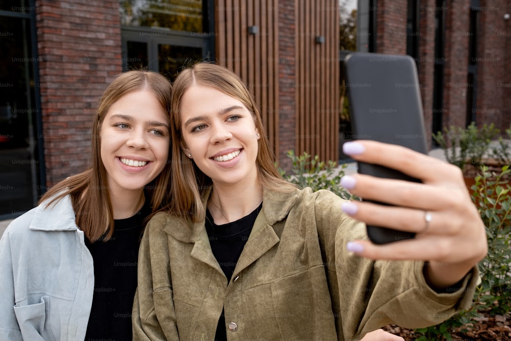 Dos lindas chicas con cabello rubio haciendo selfie contra un edificio moderno al aire libre