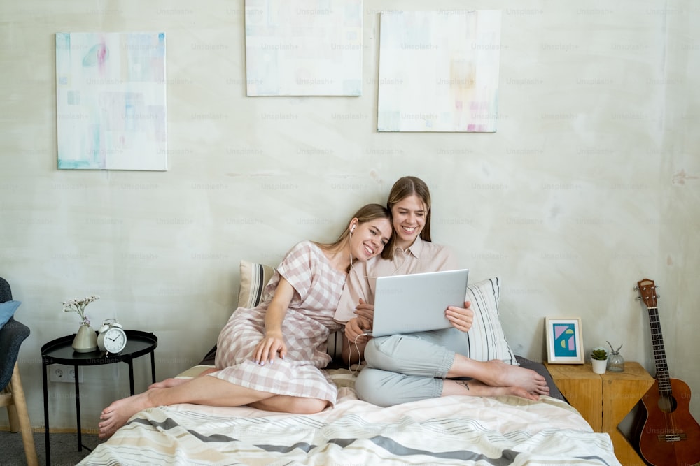 침대에서 온라인 영화를 보고 있는 노트북을 들고 있는 행복하고 다정한 두 십대 소녀