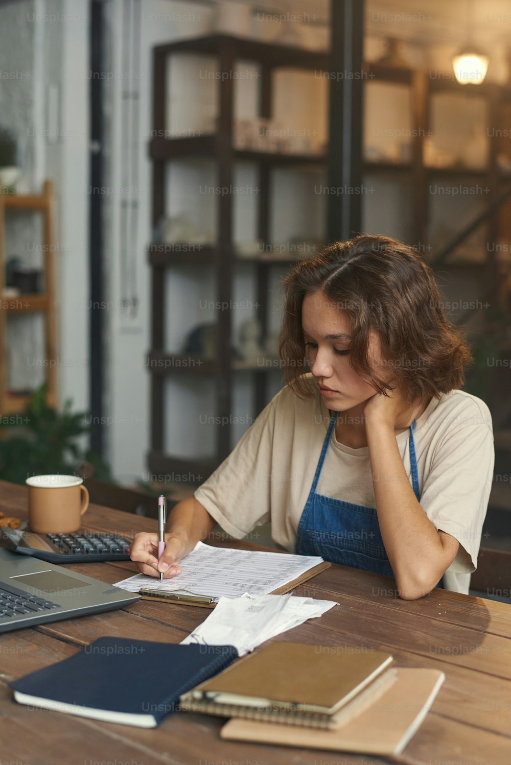 Ocupada propietaria sentada en una mesa de madera y tomando notas en papeles mientras trabajaba con las finanzas en la tienda de cerámica