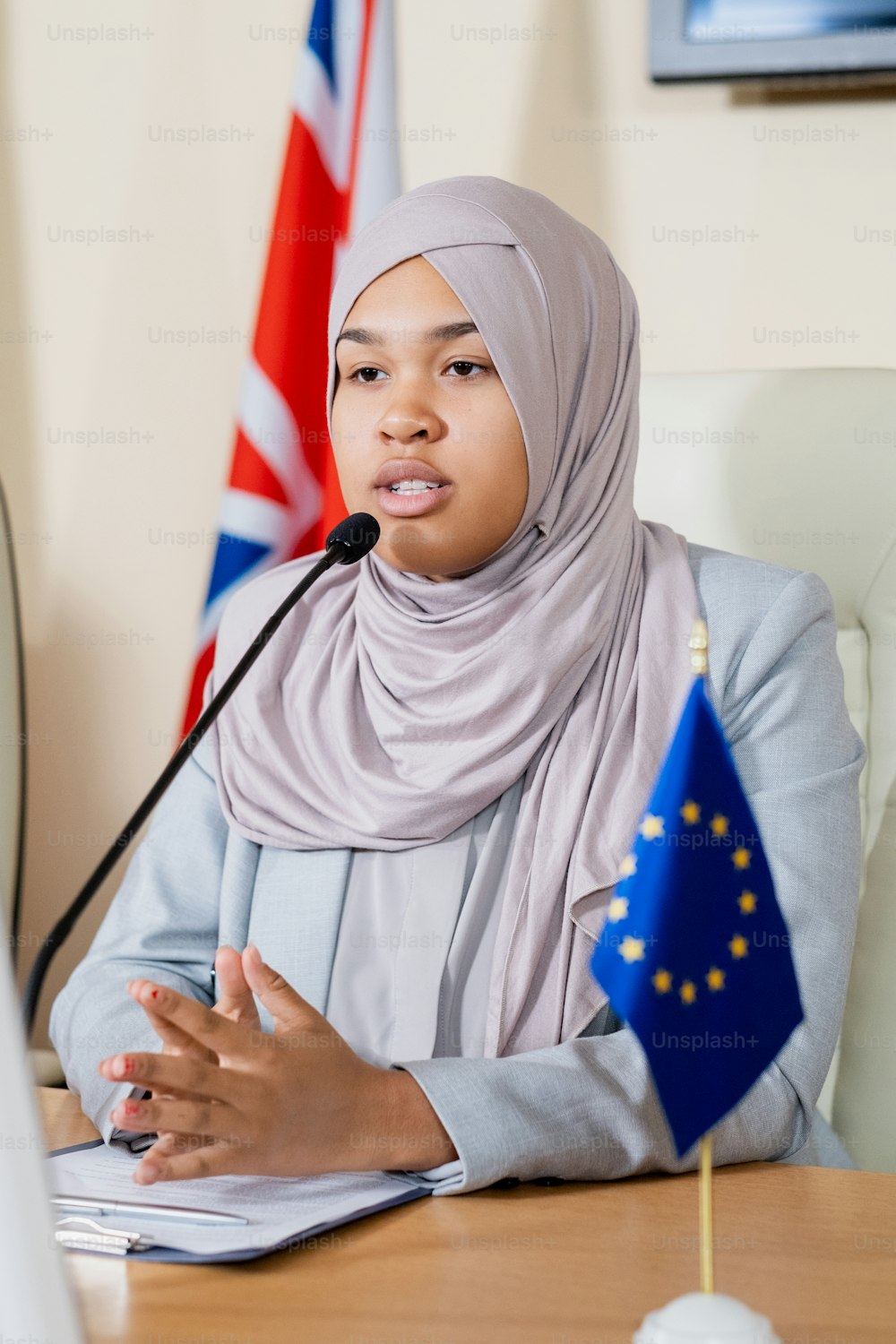 Confident muslim representative of European Union in hijab touching tips of fingers while speaking into microphone at congress