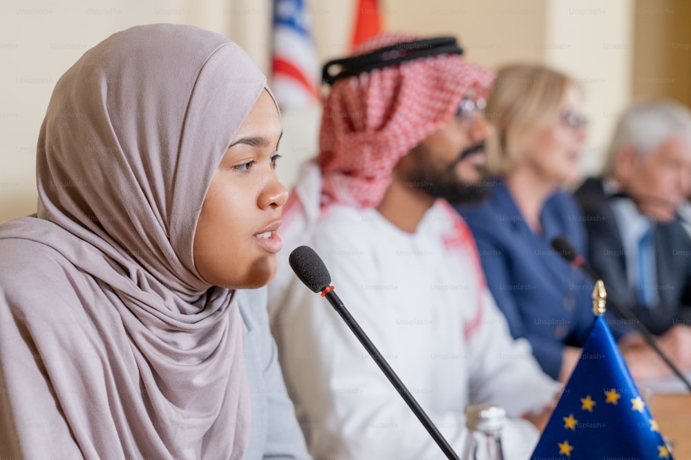 Selbstbewusste junge muslimische Politikerin im Hijab, die in das Mikrofon spricht, während sie die Frage des Journalisten beantwortet