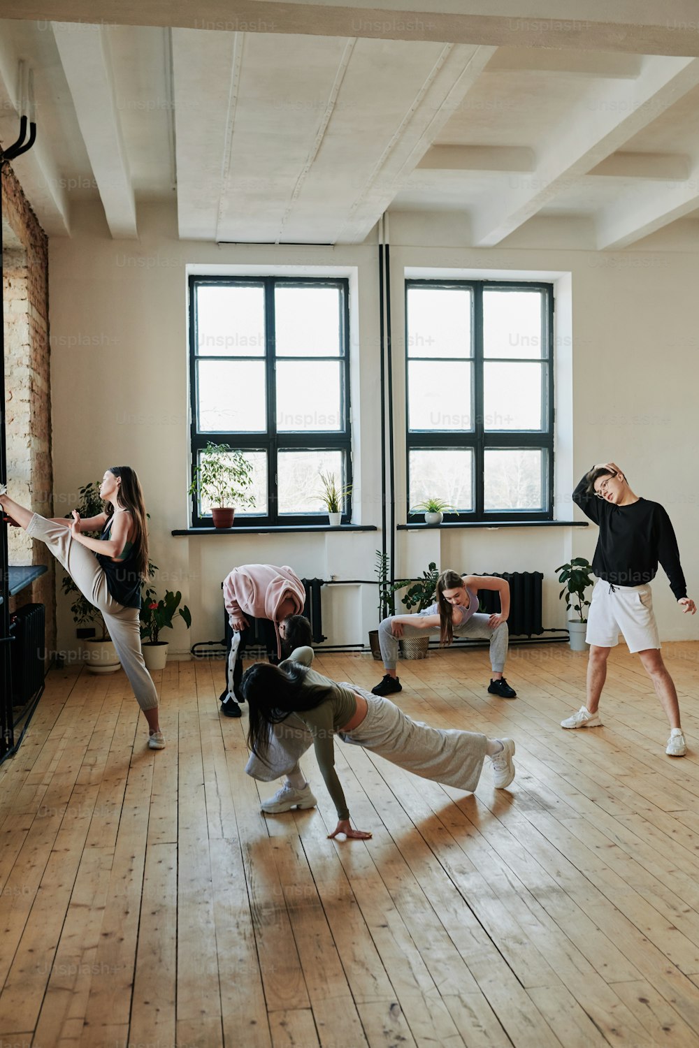 Group of adolescent people in activewear doing warmup exercises on wooden floor of dance hall or studio of modern dancing