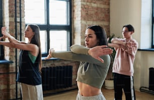 Two active teenage girls and guy crossing stretched arms in front of chest while training and repeating new movements of vogue dancing