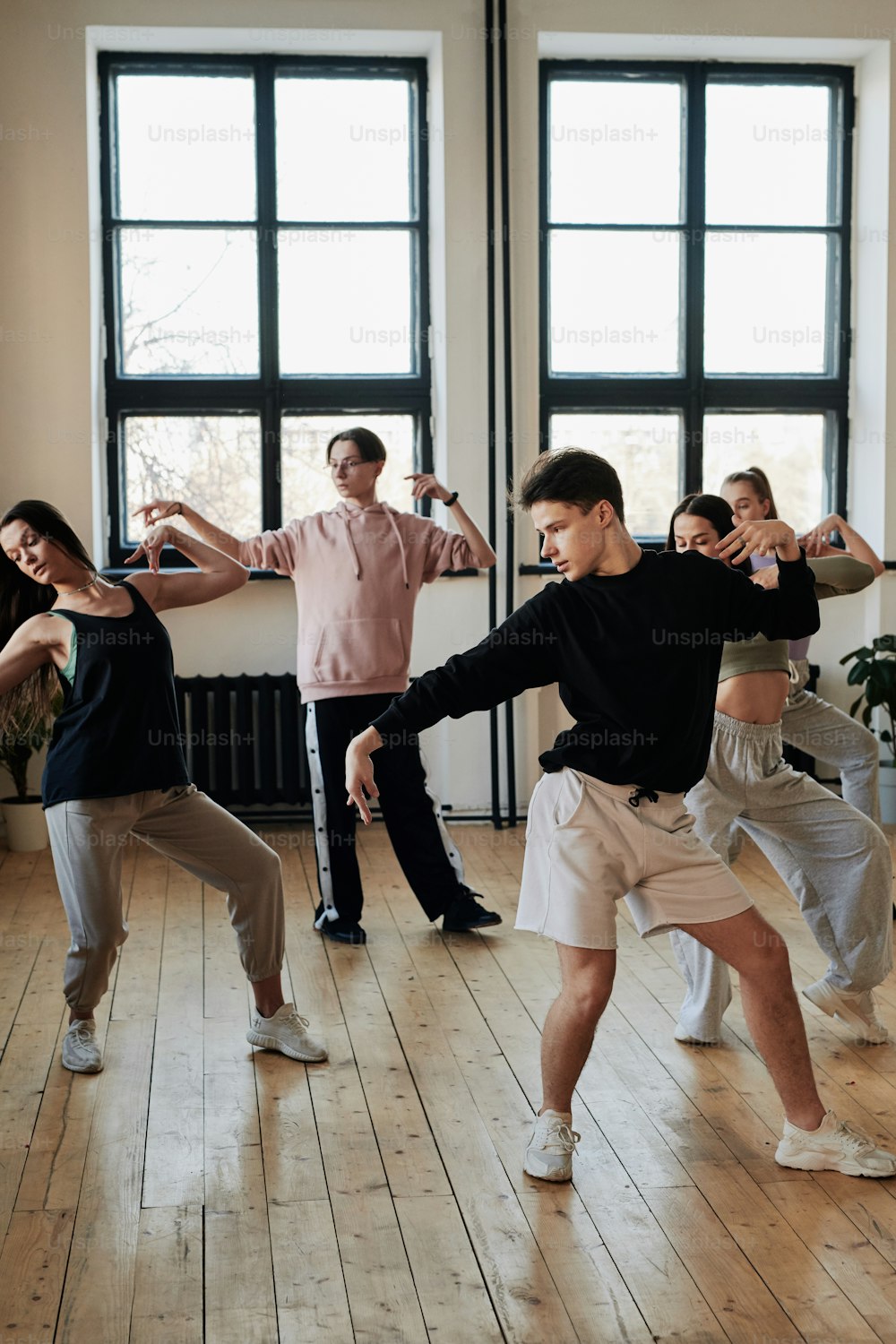 Gruppo di ragazzi adolescenti e ragazze in activewear che eseguono la danza della moda nello studio del loft mentre ripetono l'esercizio dopo il loro leader