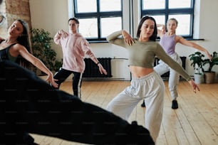 Mädchen und Teenager in Sportkleidung, die Tanzübungen nach ihrem Ausbilder oder Leiter während des Trainings im geräumigen Loft-Studio wiederholen