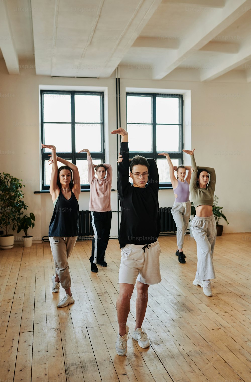 Young teenage male leader of performance group showing vogue dance exercises to group of girls and guy during training in studio