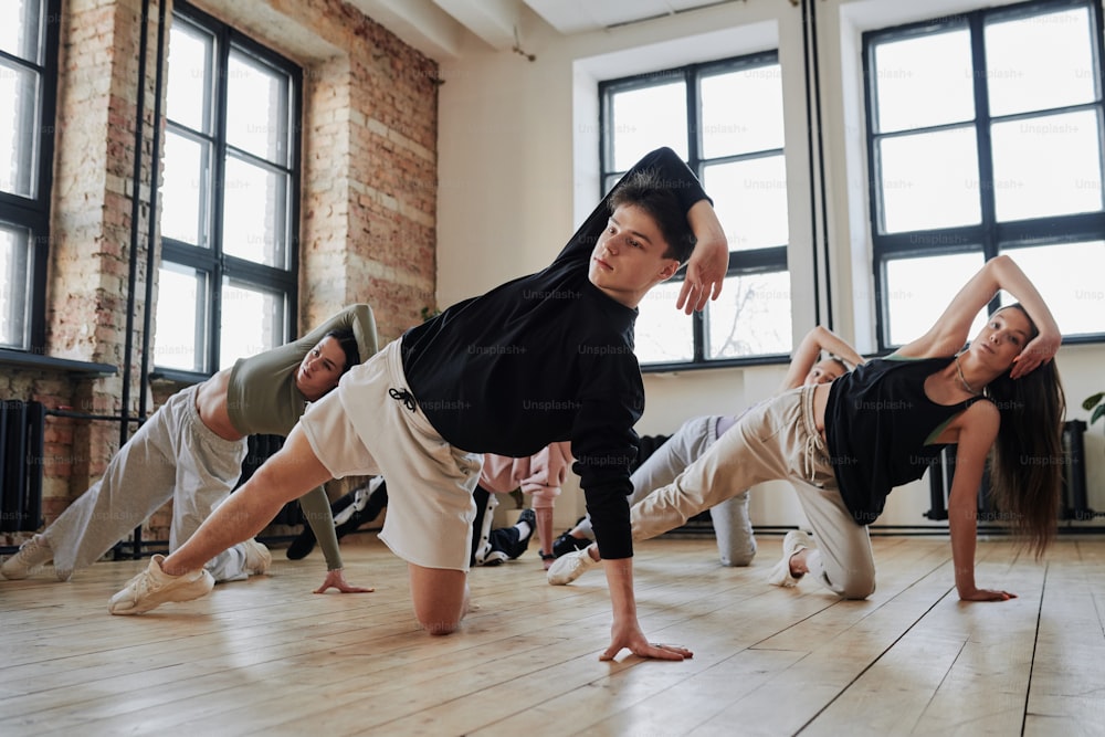 Instructor of vogue dance performance group showing new movements to teenagers in activewear during training in loft studio