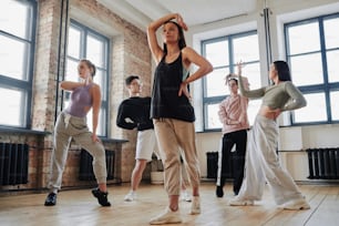 流行のダンスの新しい動きを学ぶダンスグループの前に立つ頭の上に腕を上げた若い女性パフォーマー