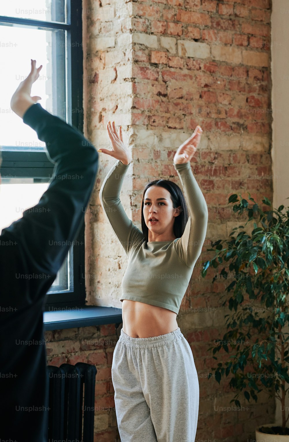 Junge weibliche Ausbilderin in Activewear, die dem männlichen Tänzer während des Trainings Ratschläge gibt, während sie mit erhobenen Armen vor ihm steht