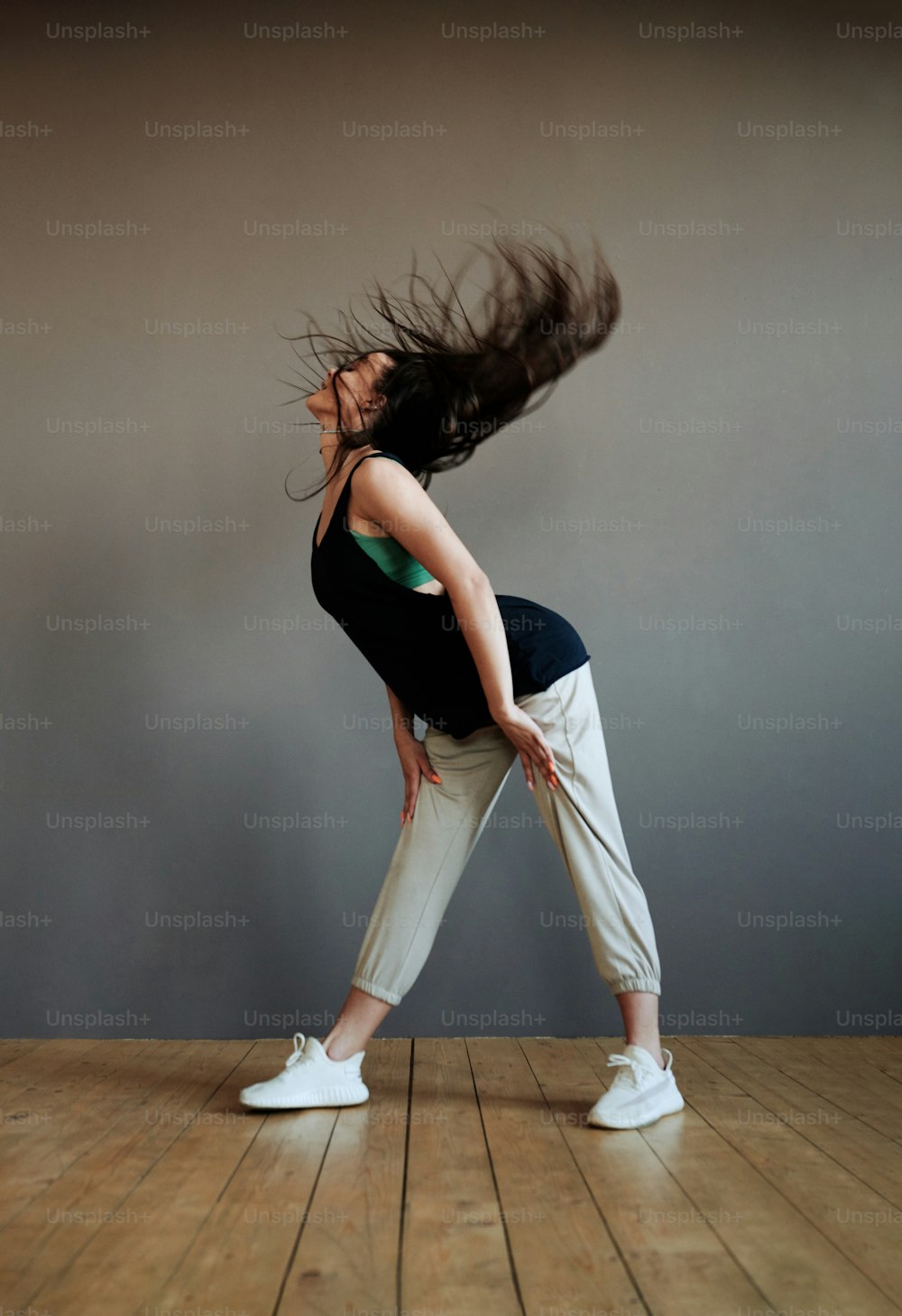 Artiste adolescente contemporaine en tenue active pratiquant un exercice de danse vogue tout en s’entraînant contre un mur gris en studio
