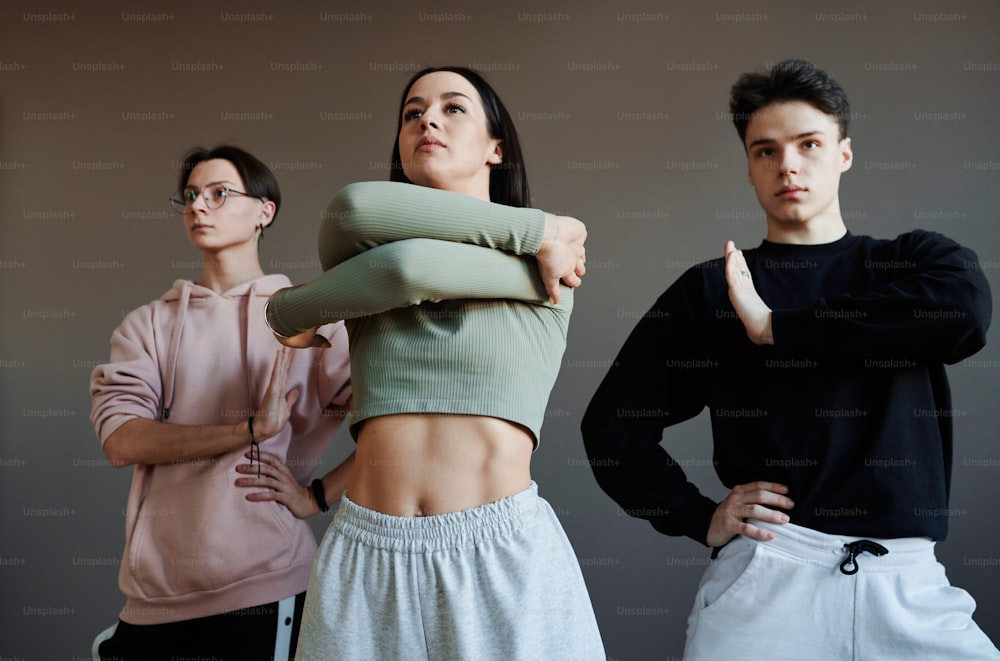 Tre millennial attivi che tengono le braccia davanti a sé durante il ballo di moda mentre si allenano o si esibiscono in studio moderno